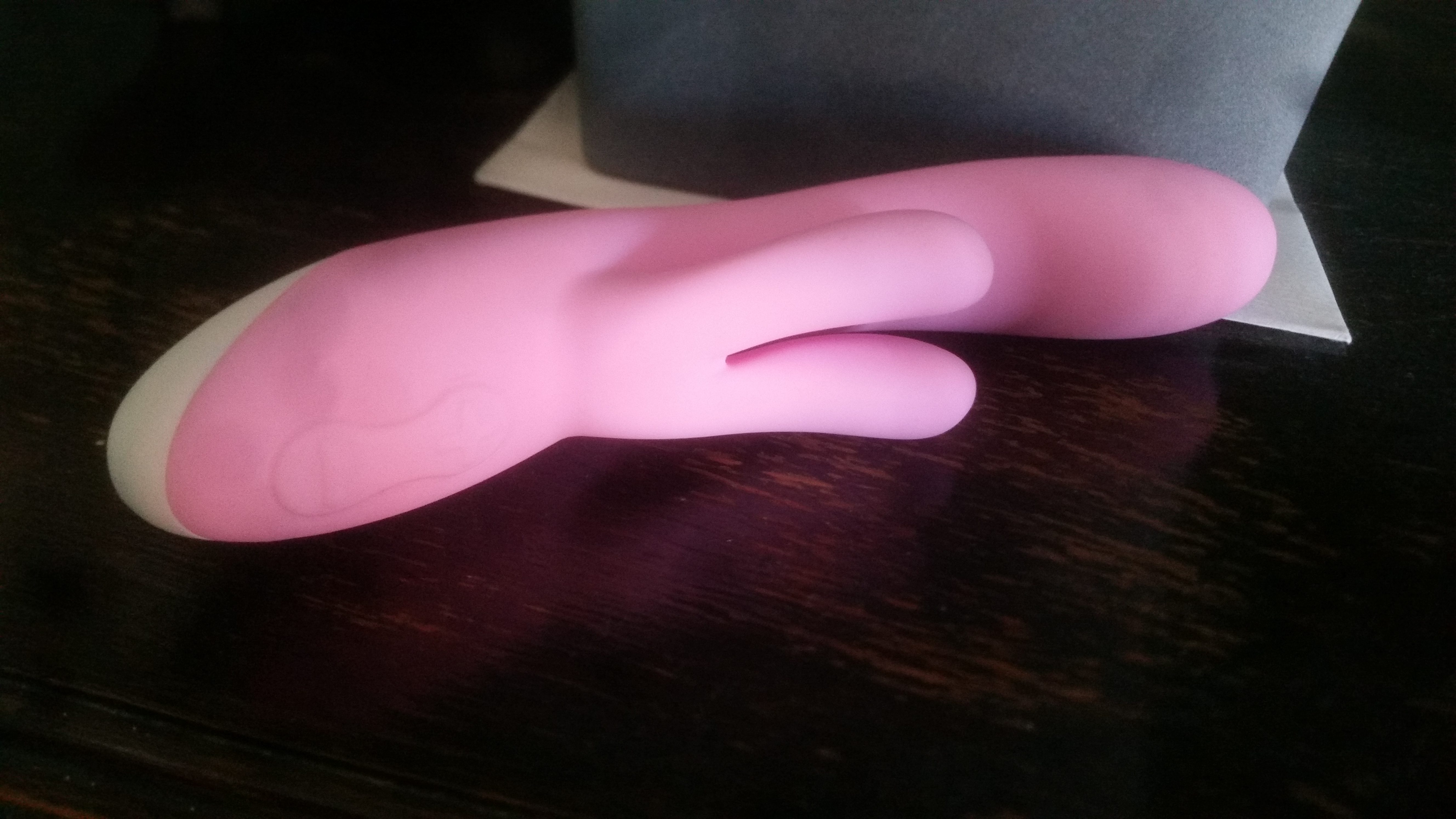 A pink rabbit vibrator lying on a dark wood surface.