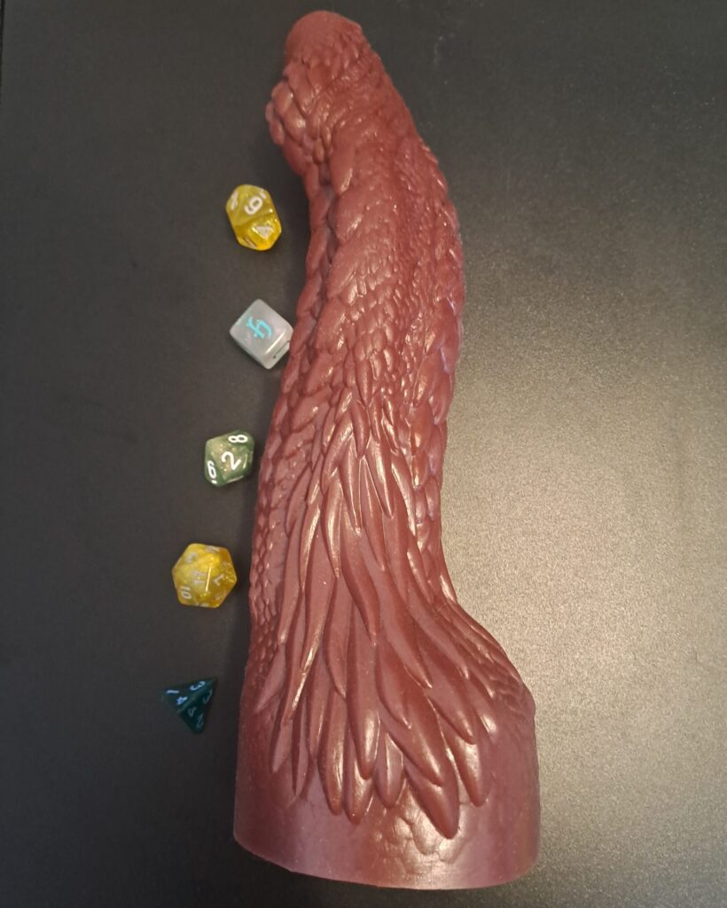 Dildos & Dragons dildo lying on black surface surrounded by D&D dice