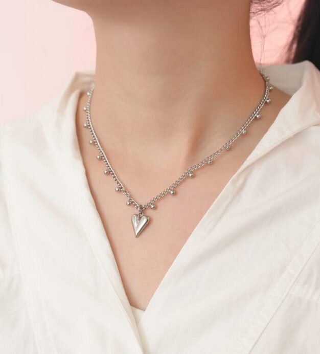 A woman wearing a silver necklace with a heart design as a subtle day collar